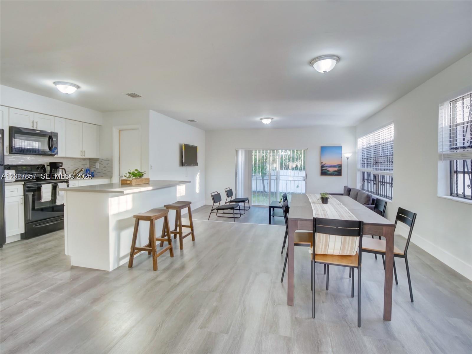 An open-concept kitchen and dining area features white cabinetry, a breakfast bar, and wood-look flooring — 1141 NW 75th St, Miami FL 33150, MIAMI, FL