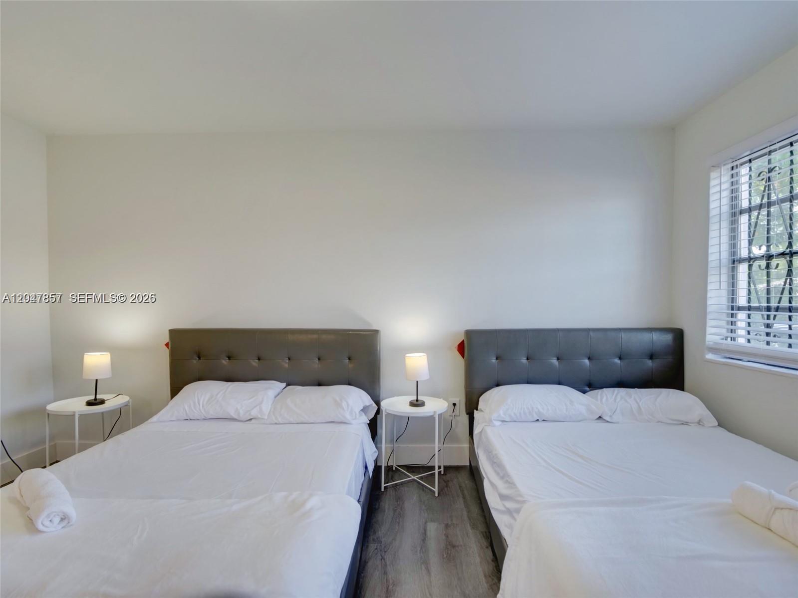 A bedroom features two beds with gray tufted headboards, white bedding, and two small side tables — 1141 NW 75th St, Miami FL 33150, MIAMI, FL