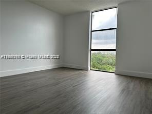 An empty room with white walls, wood-look flooring, and a large window overlooking trees — 13499 Biscayne Blvd # 801, North Miami FL 33181, NORTH MIAMI, FL