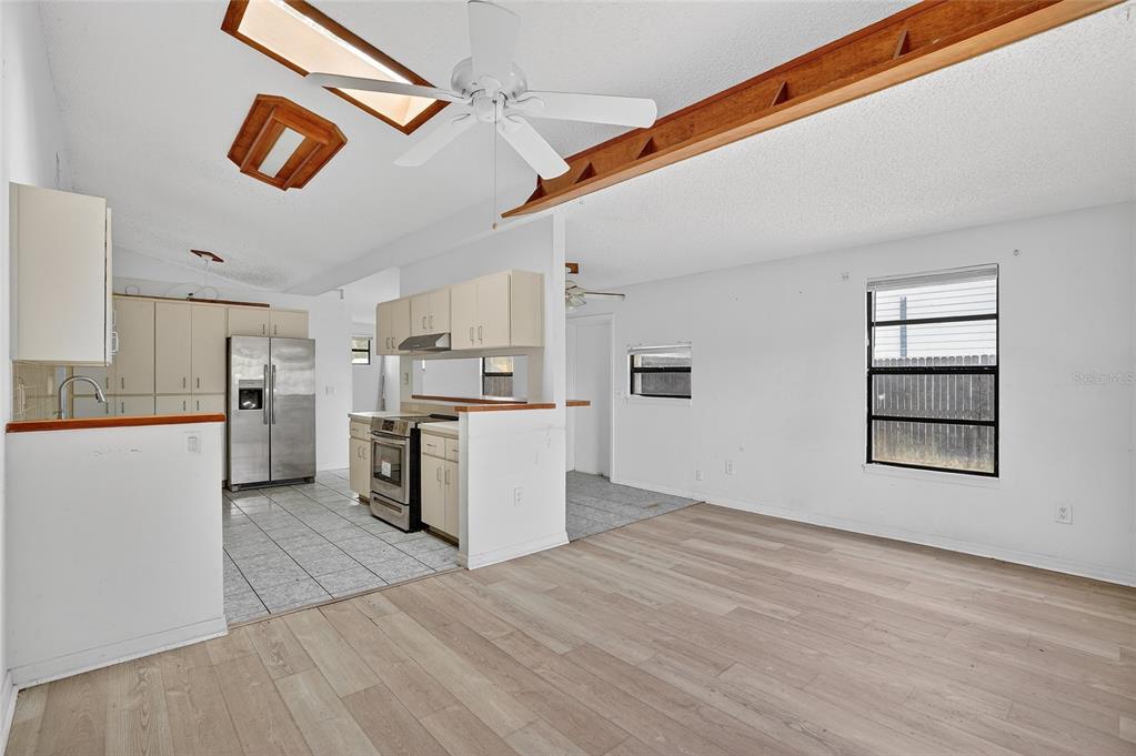 An open-concept kitchen and living area feature light wood flooring, white cabinets, and vaulted ceilings — 4320 44TH STREET N, ST PETERSBURG, FL