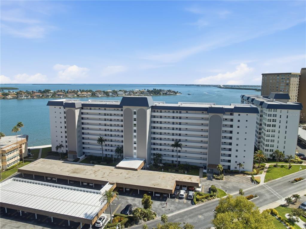 An aerial view shows a multi-story apartment building with a parking structure near the water — 5108 BRITTANY DRIVE S UNIT 506, ST PETERSBURG, FL