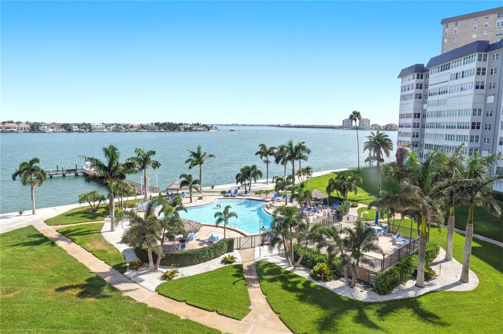 An aerial view of a waterfront swimming pool area with palm trees and a high-rise building — 5108 BRITTANY DRIVE S UNIT 506, ST PETERSBURG, FL