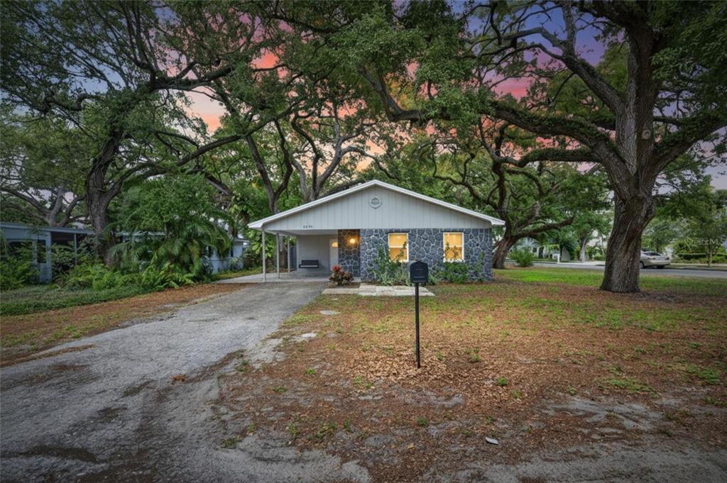 A single-story house with a stone facade and a carport sits under large oak trees — 5326 S RUSSELL STREET, TAMPA, FL