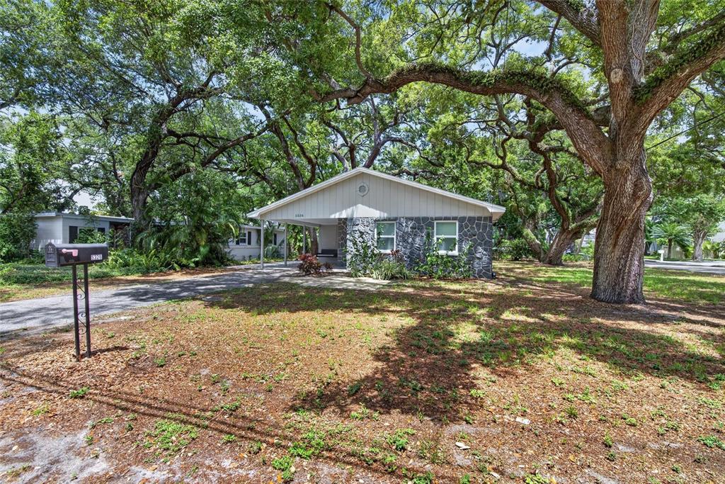 A single-story house with a stone facade and a carport sits under large oak trees — 5326 S RUSSELL STREET, TAMPA, FL