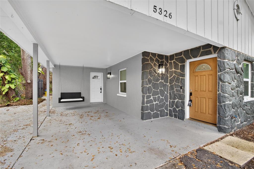 A covered carport features a hanging swing, a white door, and a stone-accented entryway — 5326 S RUSSELL STREET, TAMPA, FL