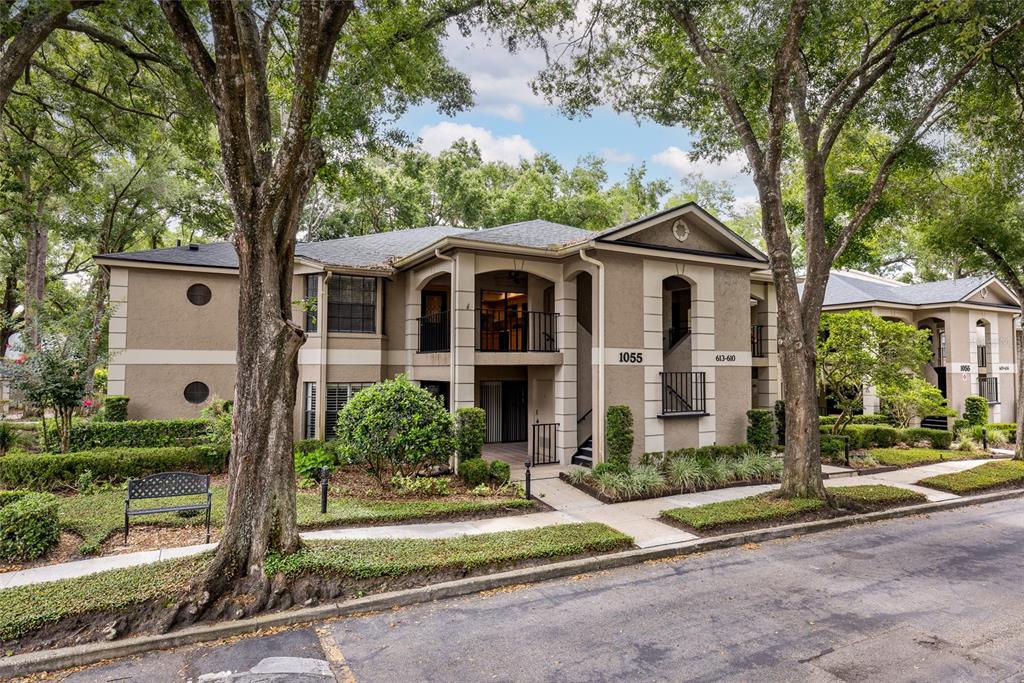 A two-story apartment building exterior with beige stucco walls, dark trim, and surrounding trees — 1055 KENSINGTON PARK DRIVE UNIT 613, ALTAMONTE SPRINGS, FL