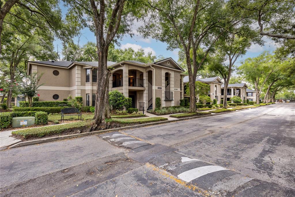 A two-story apartment building with tan stucco siding sits along a tree-lined street — 1055 KENSINGTON PARK DRIVE UNIT 613, ALTAMONTE SPRINGS, FL