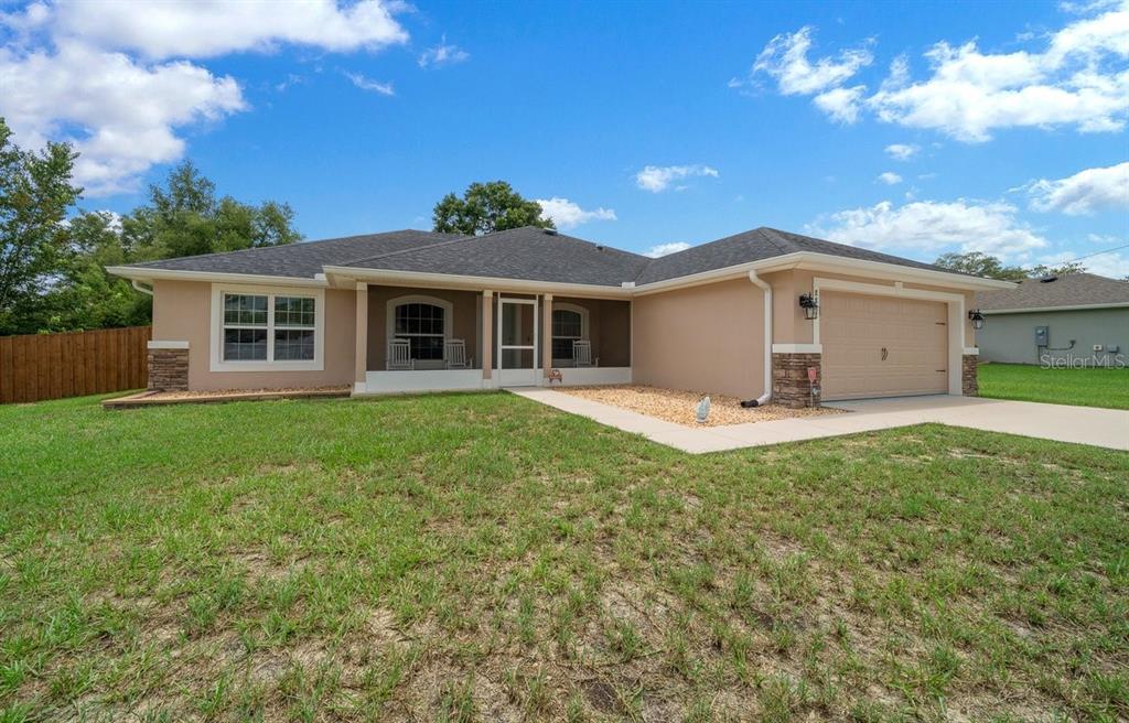 A single-story house with a tan stucco exterior, stone accents, and a two-car garage — 8828 SE 160TH PLACE, SUMMERFIELD, FL