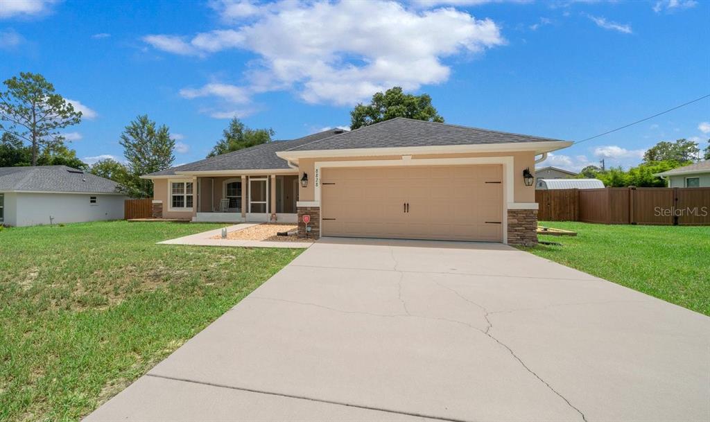 A single-story house with a tan stucco exterior, stone accents, and a two-car garage — 8828 SE 160TH PLACE, SUMMERFIELD, FL