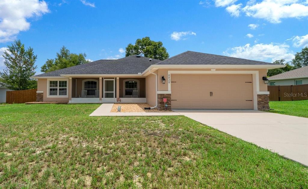 A single-story house with a tan stucco exterior, stone accents, and a two-car garage — 8828 SE 160TH PLACE, SUMMERFIELD, FL
