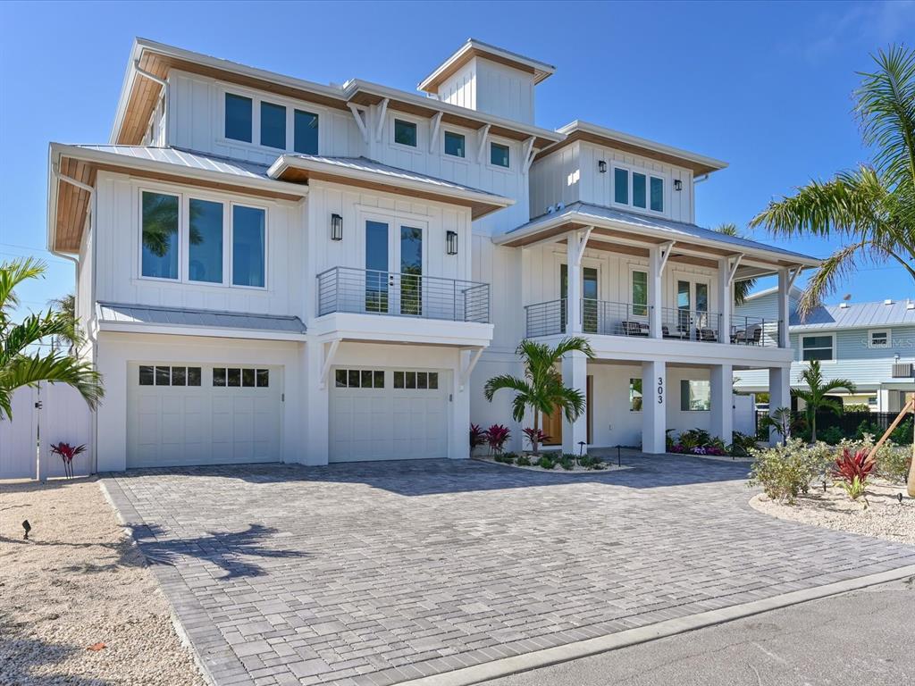 A three-story white coastal home with a paved driveway, two-car garage, and upper-level balconies — 303 55TH STREET, HOLMES BEACH, FL