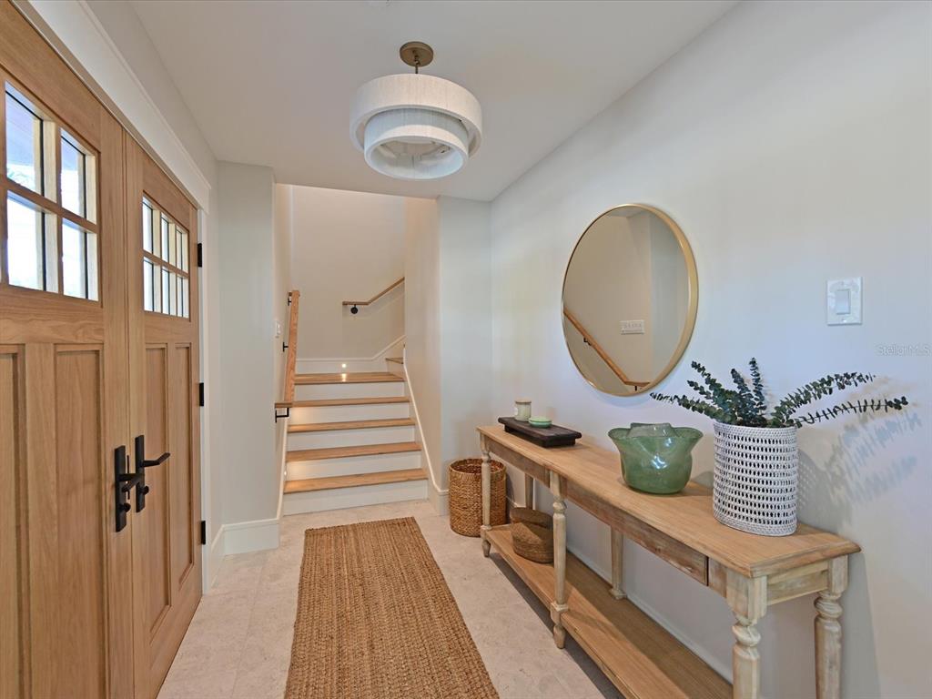 A bright entryway features a wooden console table, a round mirror, and a staircase — 303 55TH STREET, HOLMES BEACH, FL