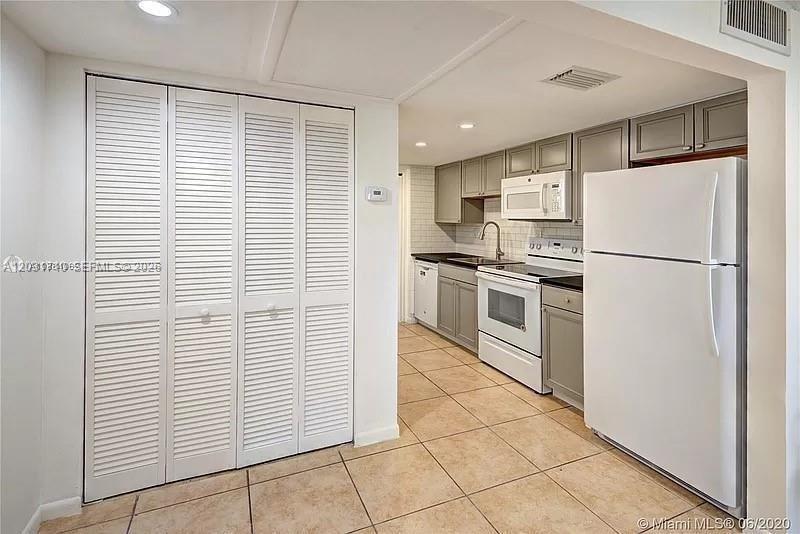 A kitchen features white louvered closet doors, light-colored tile flooring, and white appliances — 4121 NW 26th St # T14, Lauderhill FL 33313, LAUDERHILL, FL