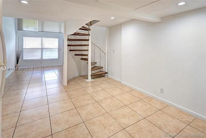 A room with beige tile flooring features a spiral staircase leading to an upper level — 4121 NW 26th St # T14, Lauderhill FL 33313, LAUDERHILL, FL