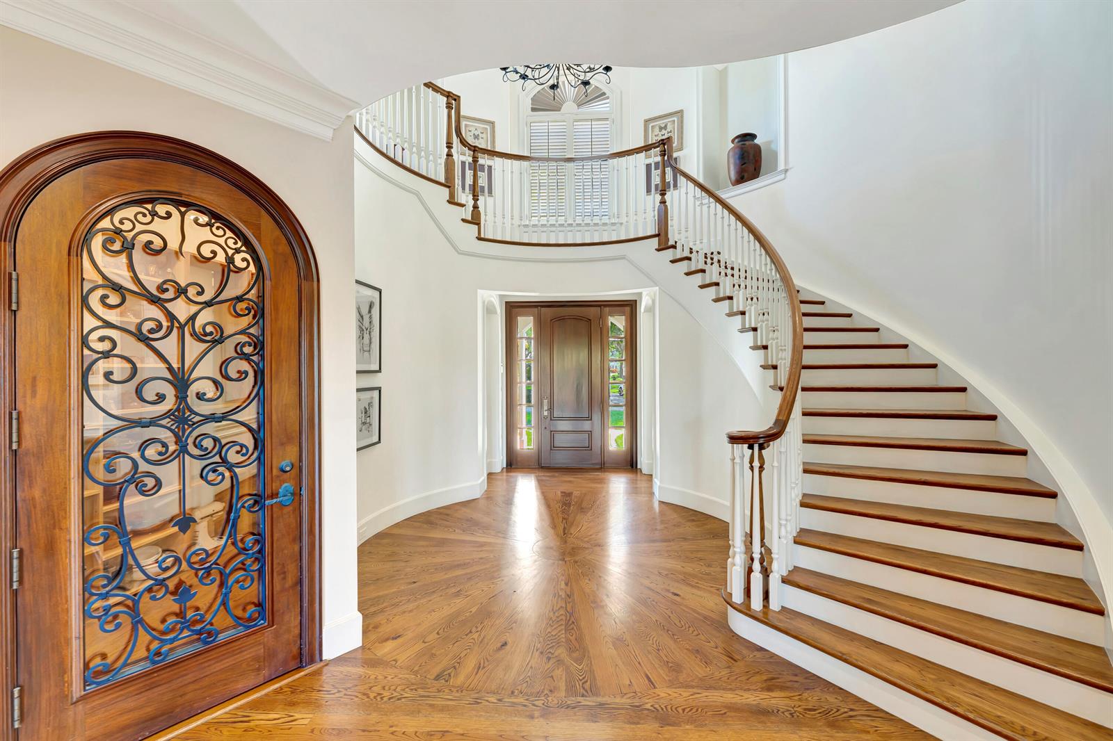 A grand foyer features a curved staircase, hardwood floors, and a decorative arched wooden door — VERO BEACH, FL