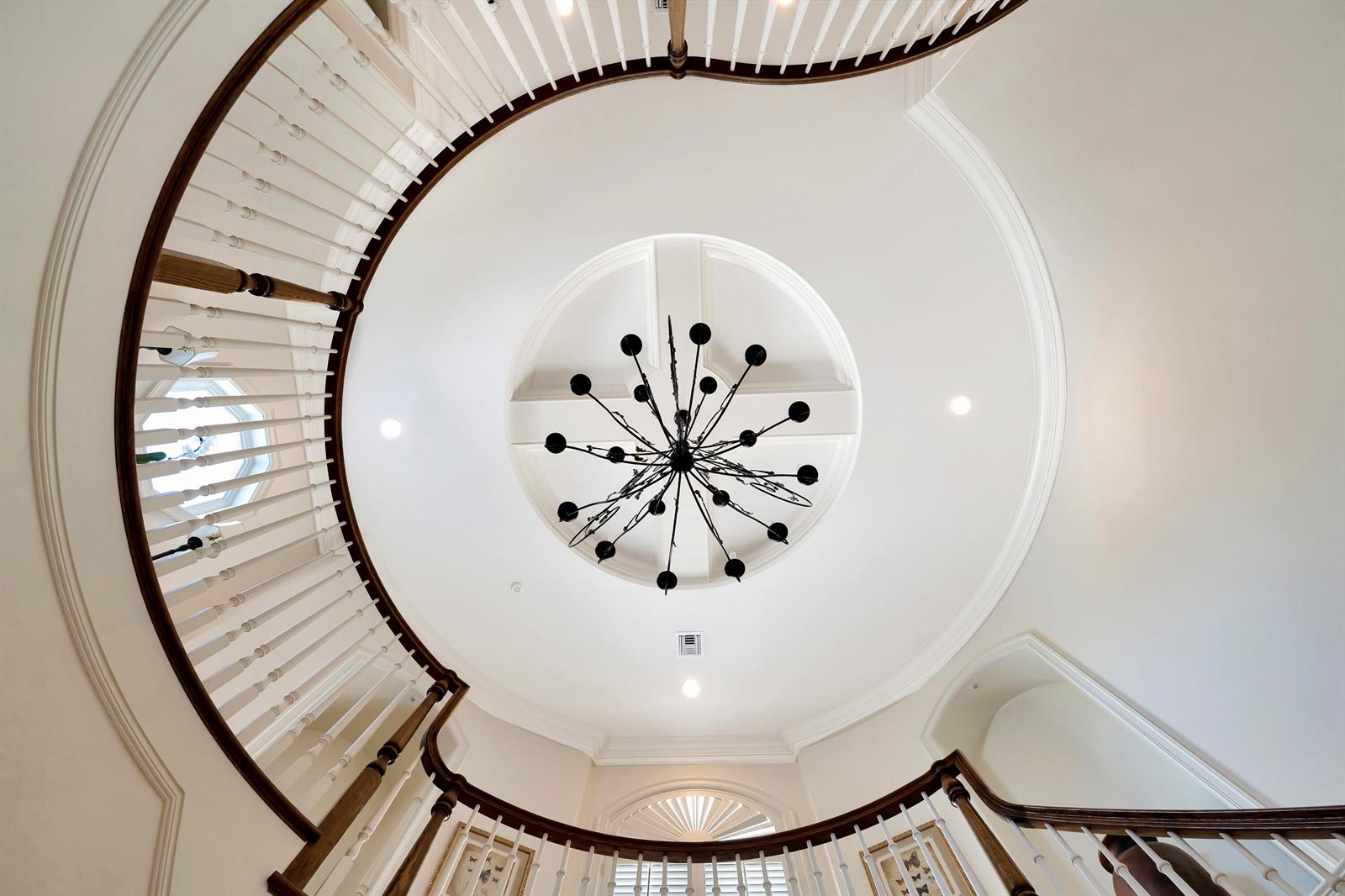 A low-angle view of a grand foyer featuring a curved staircase and a central chandelier — VERO BEACH, FL