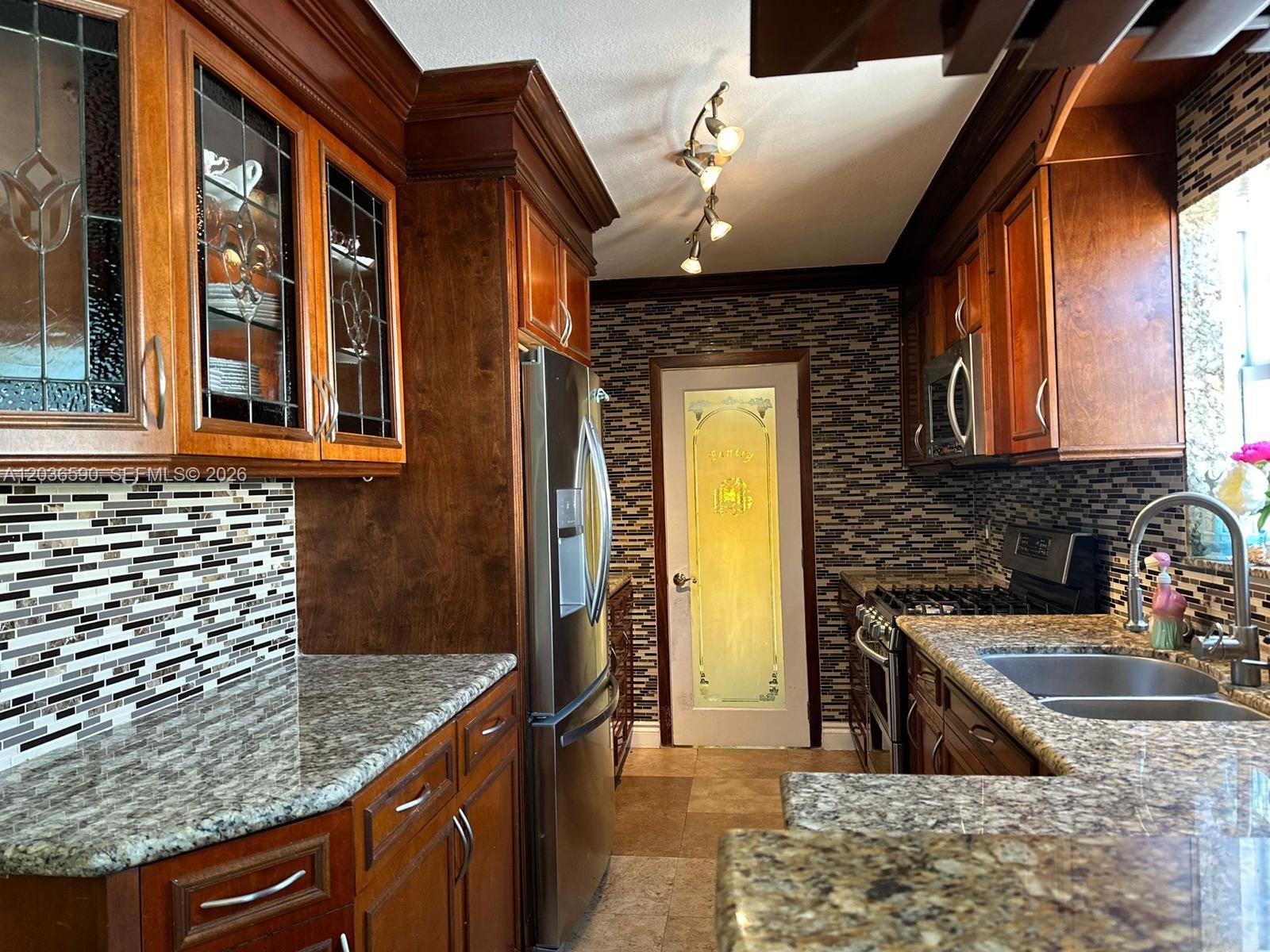 A kitchen features dark wood cabinets, granite countertops, a mosaic tile backsplash, and stainless appliances — 707 SW 3rd Ave, Hallandale Beach FL 33009, HALLANDALE BEACH, FL