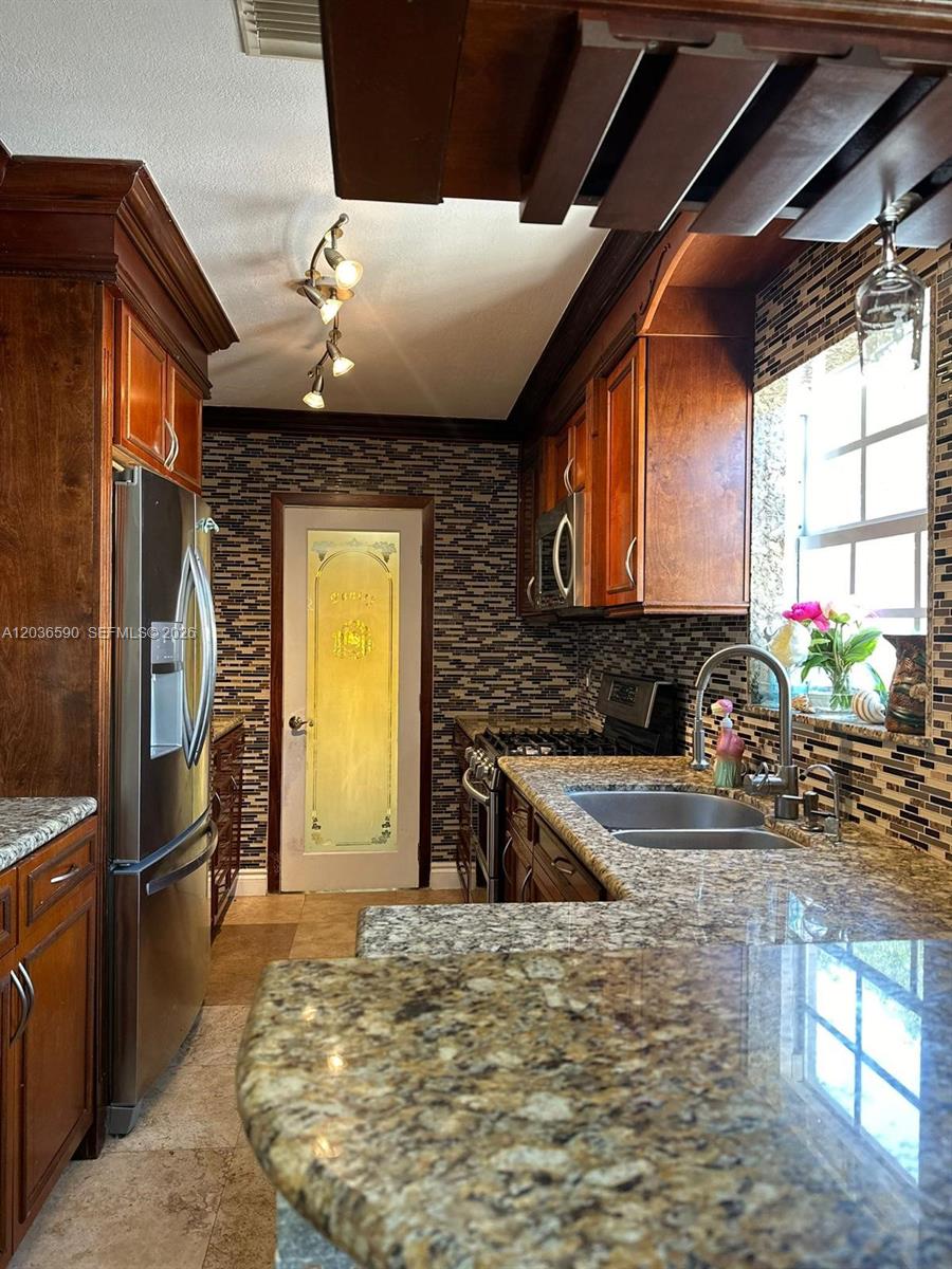 A kitchen features wood cabinets, granite countertops, a mosaic tile backsplash, and a pantry door — 707 SW 3rd Ave, Hallandale Beach FL 33009, HALLANDALE BEACH, FL