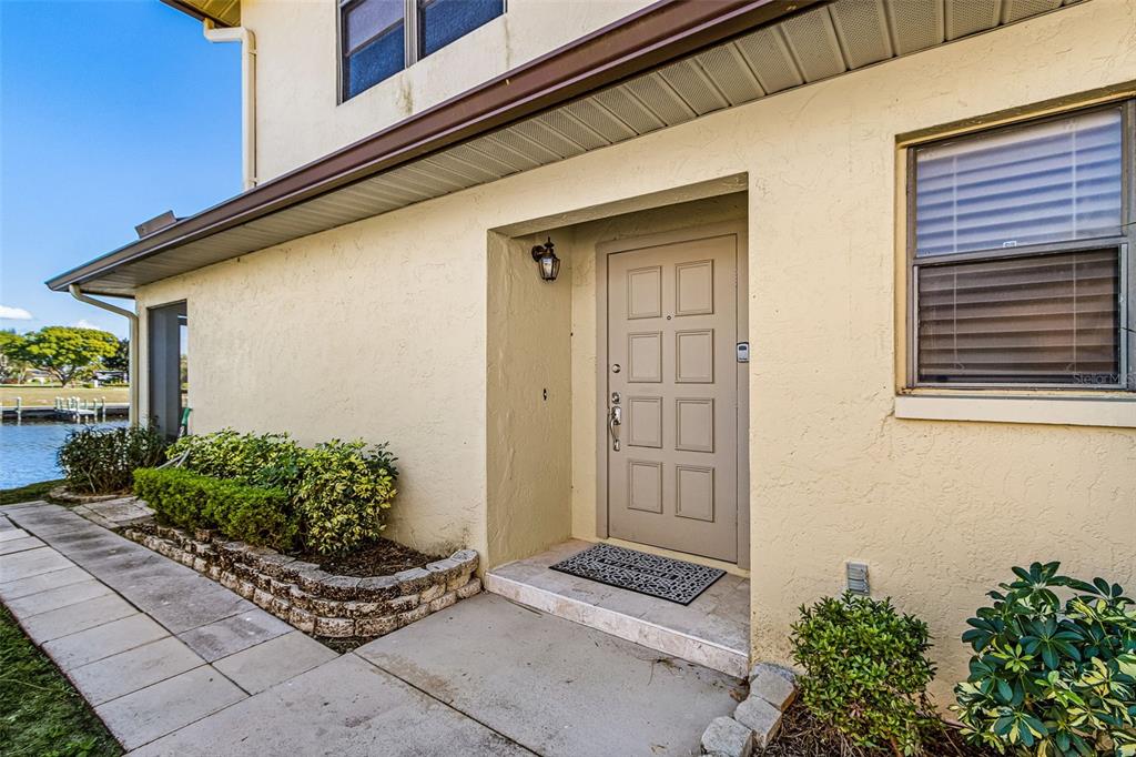 A beige exterior wall features a tan front door with eight panels and a small porch — 3831 SE 11TH PLACE UNIT 101, CAPE CORAL, FL