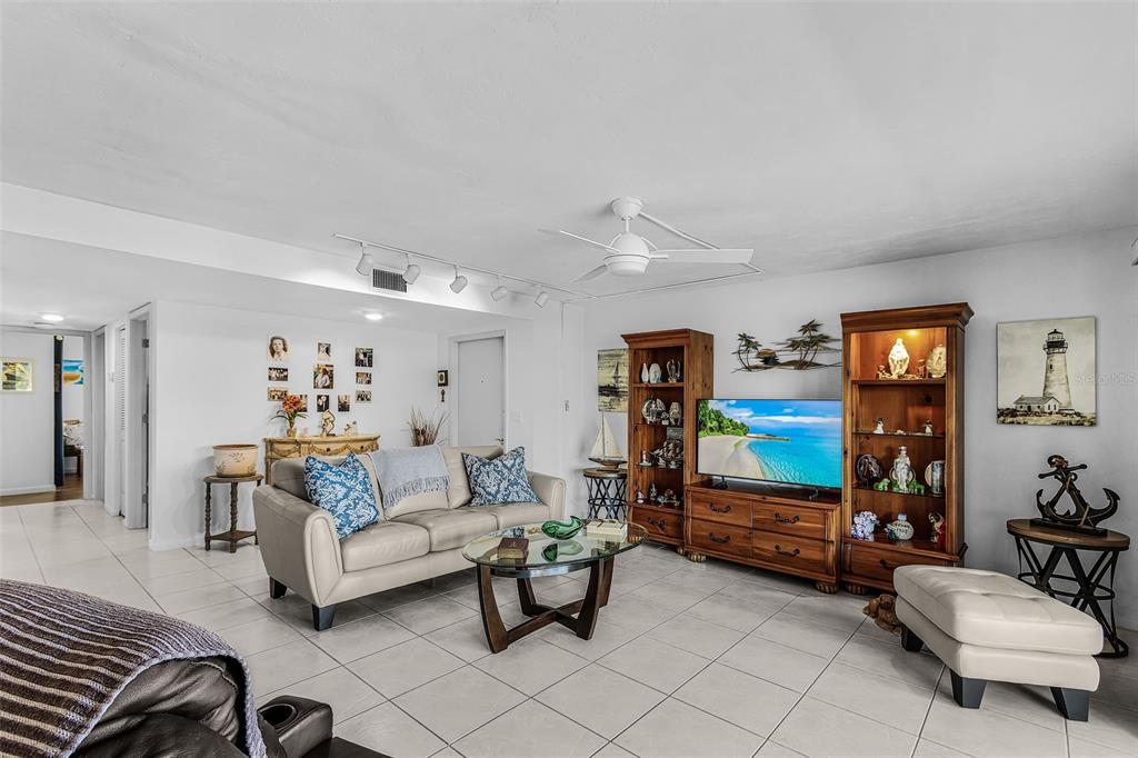 A living room features tile floors, a beige sofa, wooden shelving units, and a television — 3831 SE 11TH PLACE UNIT 101, CAPE CORAL, FL