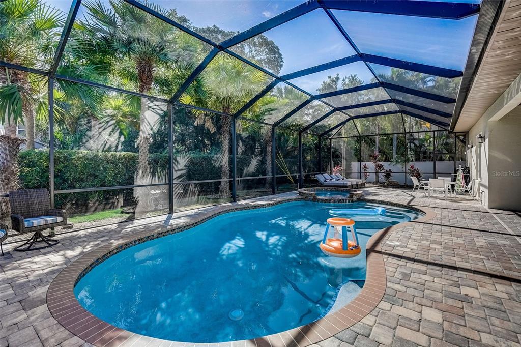 A screened-in patio features a kidney-shaped swimming pool, a hot tub, and paver decking — 125 S BLVD OF PRESIDENTS, SARASOTA, FL