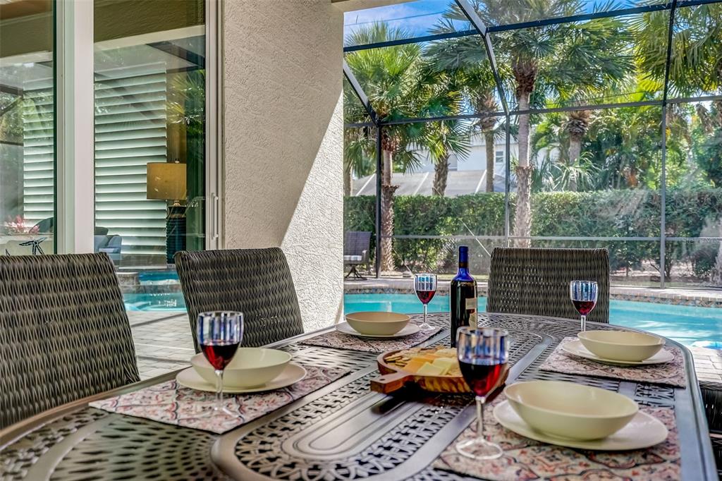 A patio dining set with wine and snacks overlooks a screened-in swimming pool and palm trees — 125 S BLVD OF PRESIDENTS, SARASOTA, FL