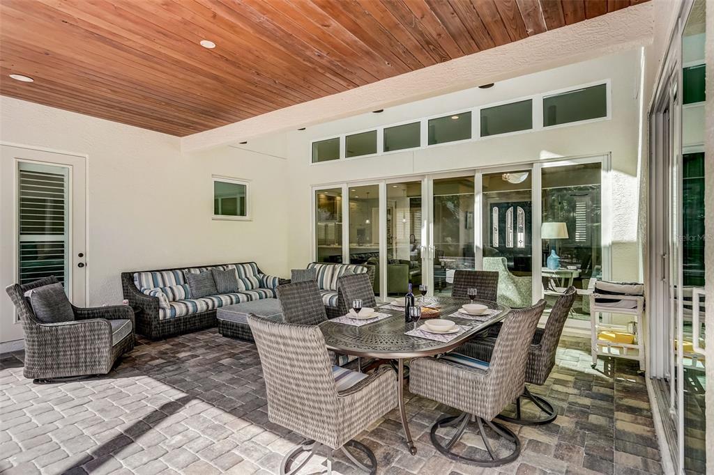 A covered patio features a dining set, outdoor sofa, and wood-paneled ceiling with sliding glass doors — 125 S BLVD OF PRESIDENTS, SARASOTA, FL