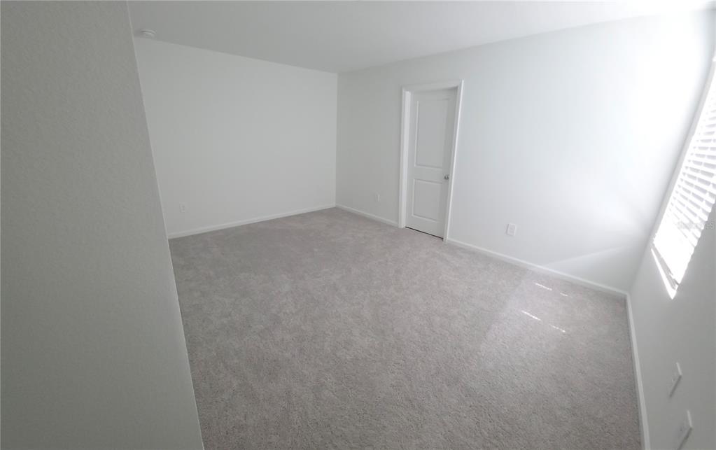 An empty bedroom features white walls, gray carpeting, a single door, and a window with blinds — 7191 SW 92ND STREET, OCALA, FL