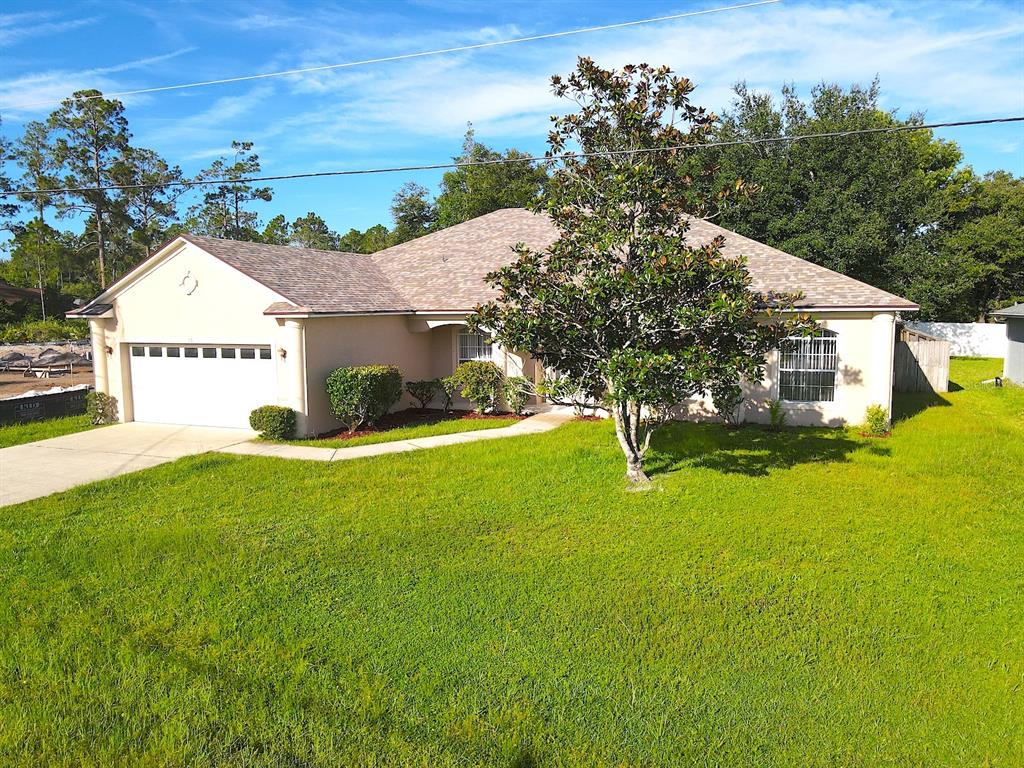 A single-story house with a white garage, beige siding, and a large tree in front — 16 ZORLOU COURT, PALM COAST, FL