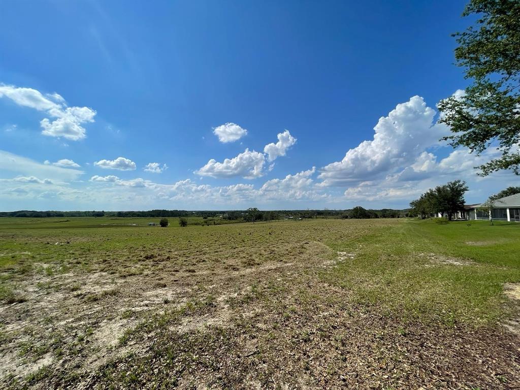 A wide, grassy, undeveloped lot under a bright blue sky with scattered clouds — Lot 2 MERCADO COURT, CLERMONT, FL