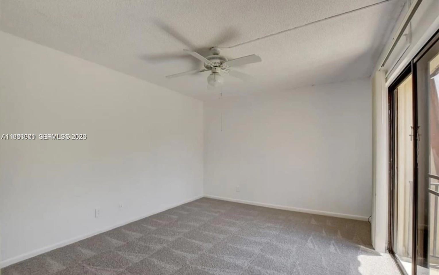 An empty room features white walls, gray carpeting, a ceiling fan, and a sliding glass door — 3103 Spanish Wells dr # 2A, Delray Beach FL 33445, DELRAY BEACH, FL