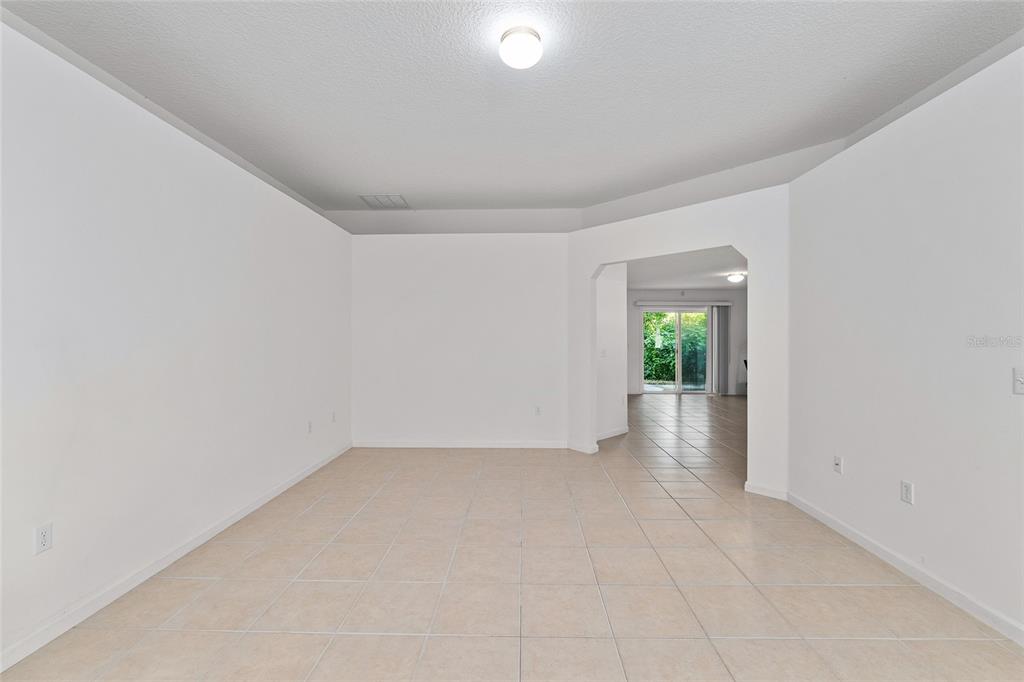 An empty room with white walls, tile flooring, and a doorway leading to a patio — 4939 NW 81ST AVENUE, GAINESVILLE, FL