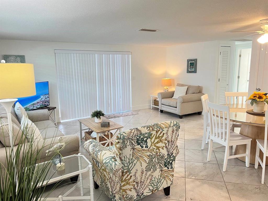 A living and dining area with tile floors, a patterned armchair, and a sliding glass door — 6154 MIDNIGHT PASS ROAD UNIT A04, SARASOTA, FL