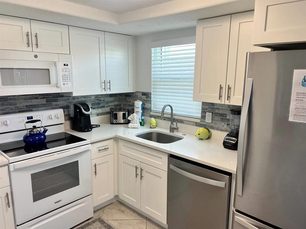A kitchen with white cabinets, stainless steel appliances, and a gray tiled backsplash — 6154 MIDNIGHT PASS ROAD UNIT A04, SARASOTA, FL