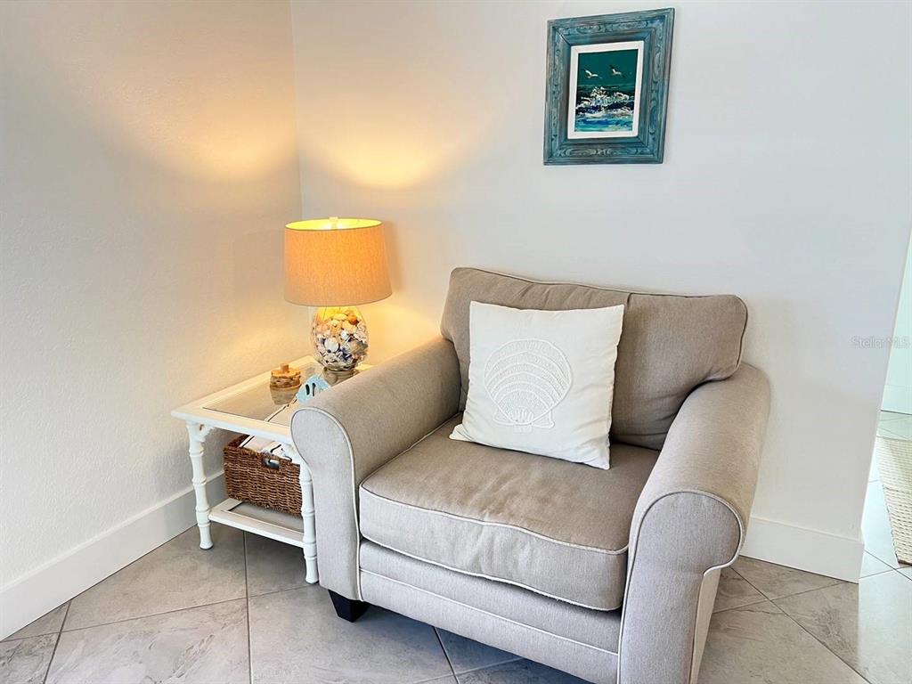 A beige armchair with a seashell pillow sits next to a side table and lamp — 6154 MIDNIGHT PASS ROAD UNIT A04, SARASOTA, FL