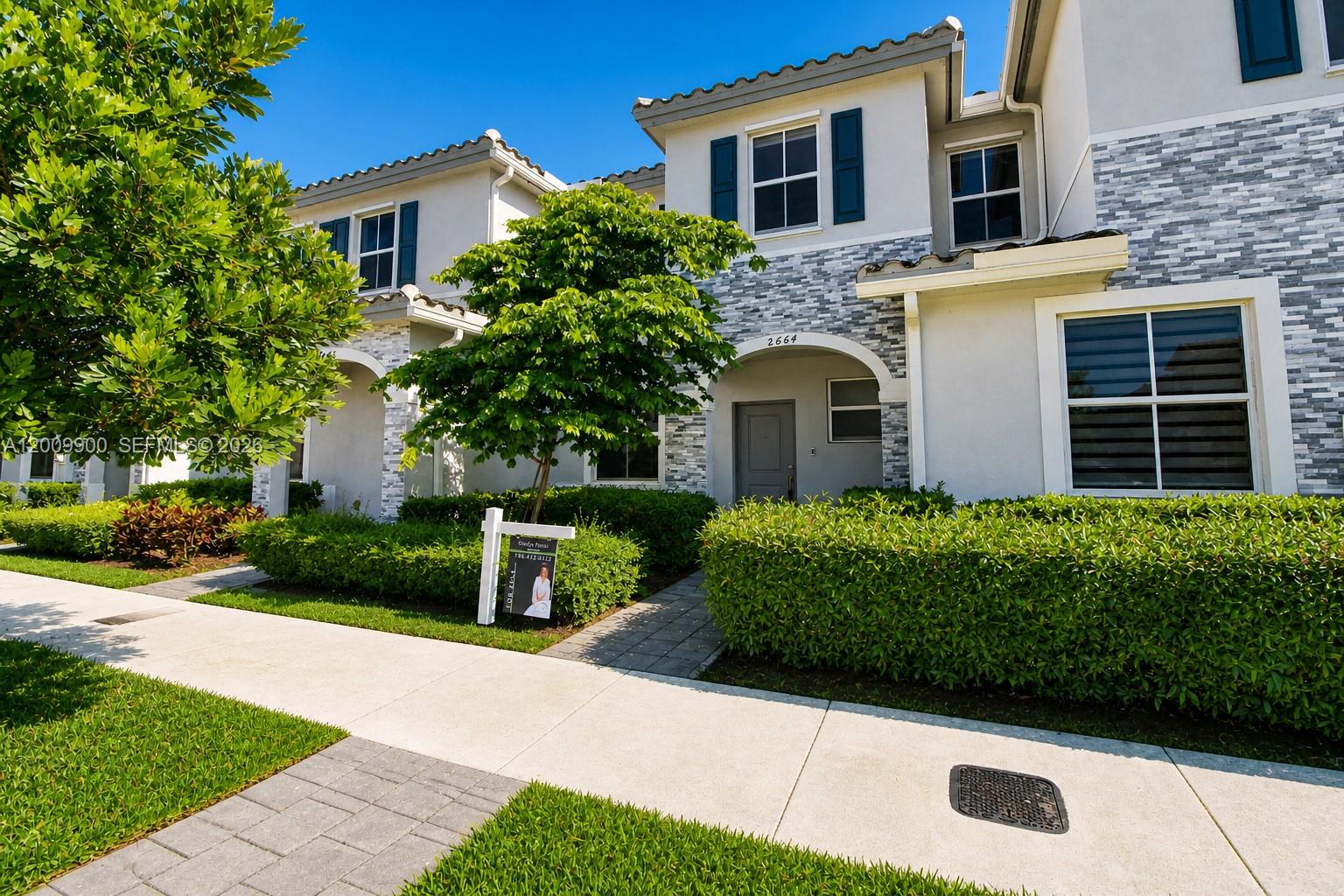 A two-story townhouse with a stone-accented facade, dark shutters, and a manicured hedge — 2664 SE 19th St, Homestead FL 33035, HOMESTEAD, FL