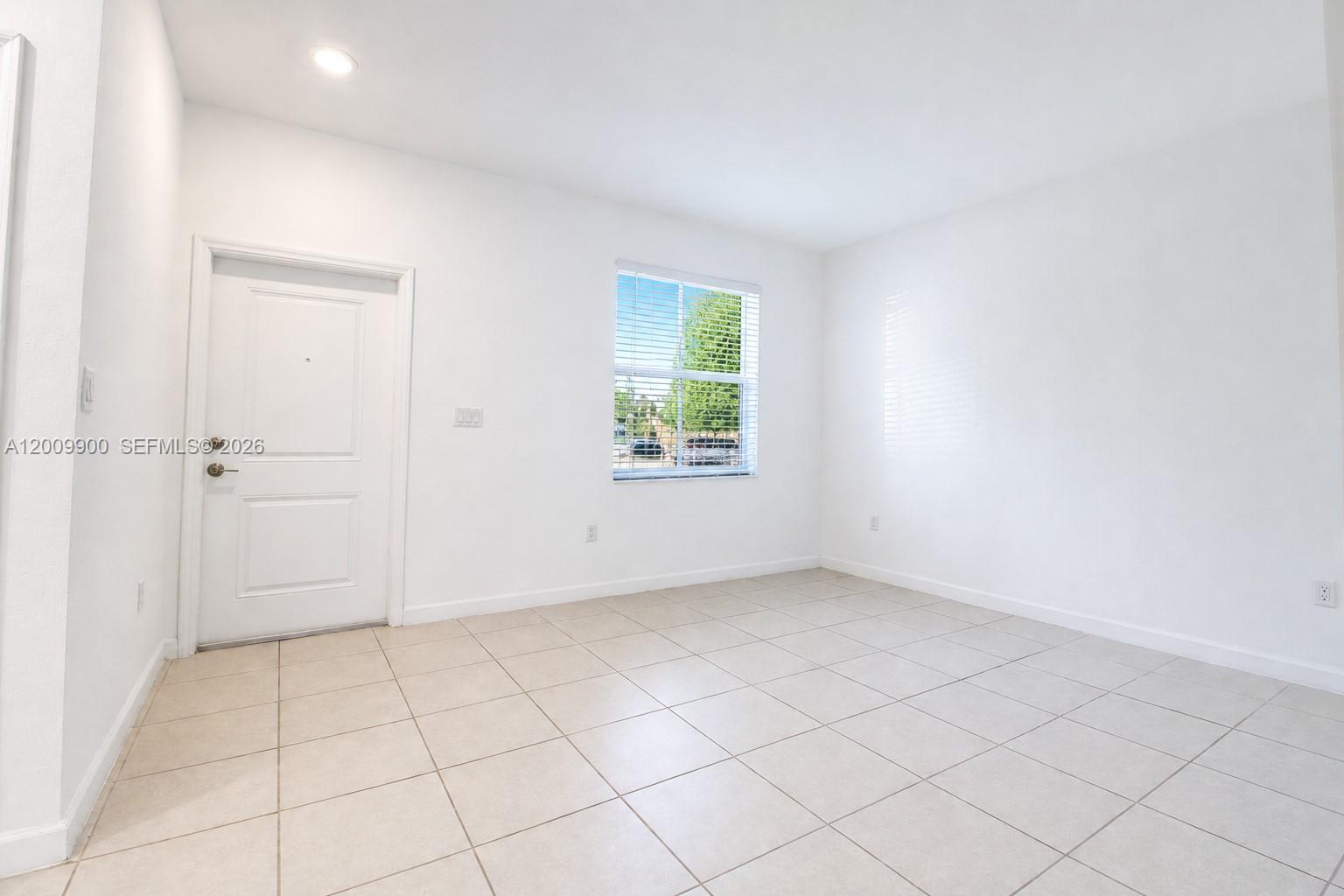 An empty room features white walls, light-colored tile flooring, a single window, and a door — 2664 SE 19th St, Homestead FL 33035, HOMESTEAD, FL