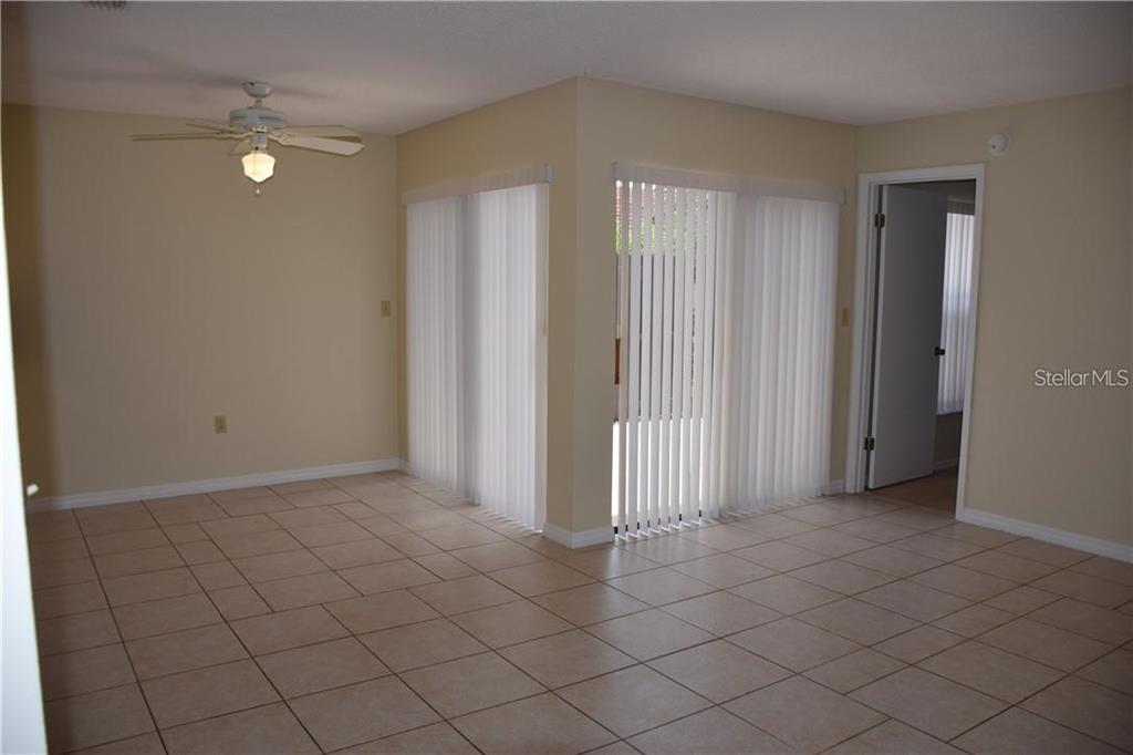 An empty room with beige tile flooring, a ceiling fan, and vertical blinds on windows — 470 HUNTER CIRCLE, KISSIMMEE, FL