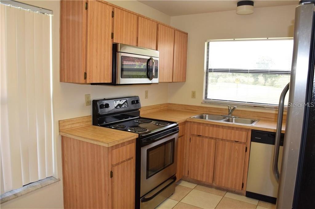A kitchen features wood-grain cabinets, black appliances, a stainless steel sink, and tiled flooring — 470 HUNTER CIRCLE, KISSIMMEE, FL