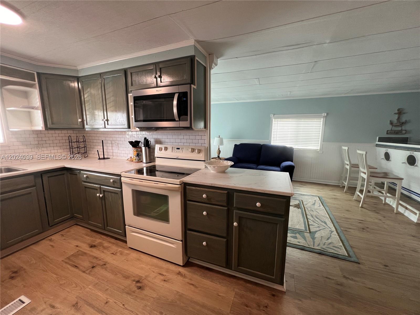 A kitchen with dark cabinets and white appliances opens into a living and dining area — 8709 SW 15th St, Davie FL 33324, DAVIE, FL