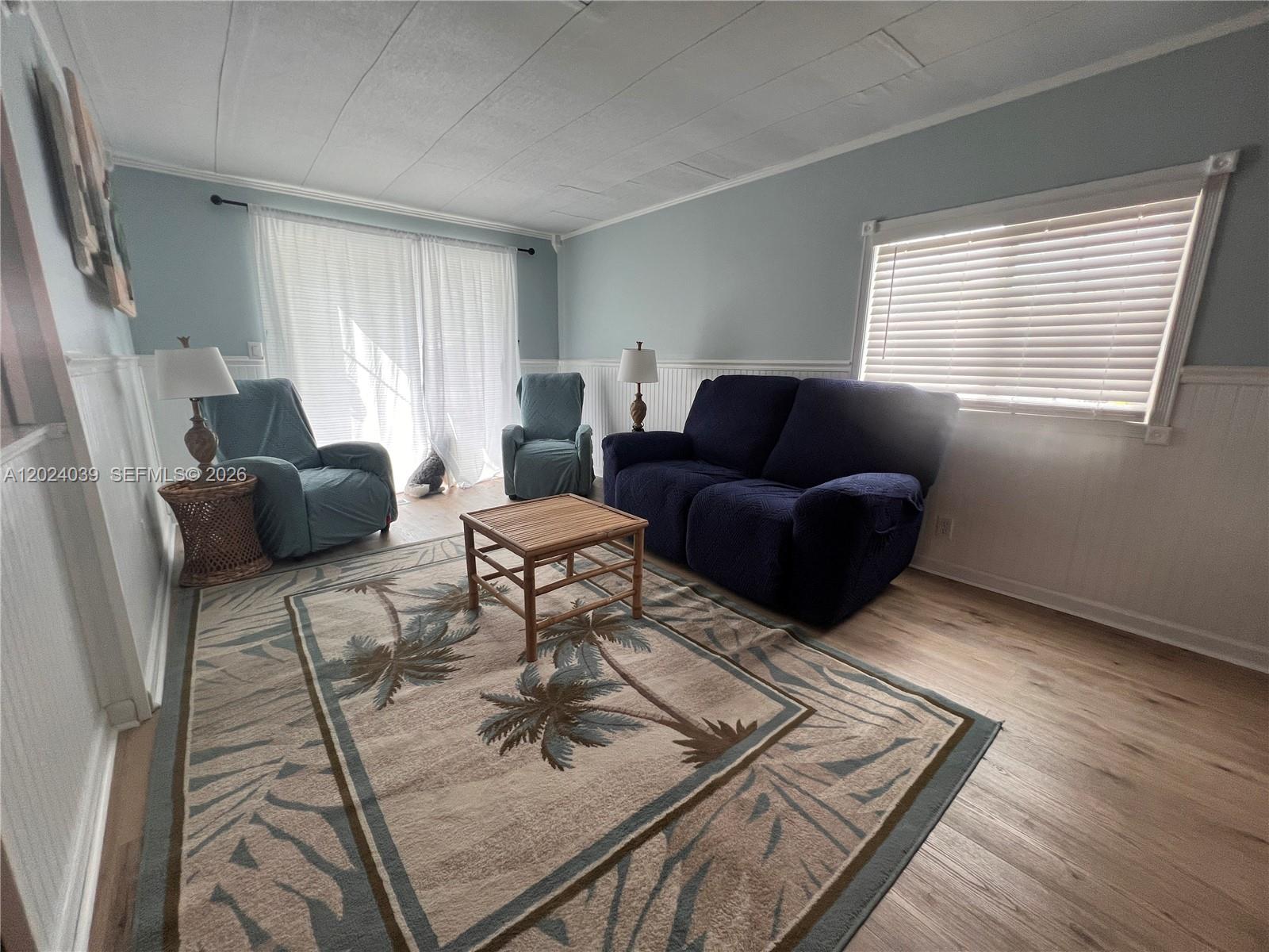 A living room features light blue walls, wainscoting, a palm-patterned rug, and blue furniture — 8709 SW 15th St, Davie FL 33324, DAVIE, FL