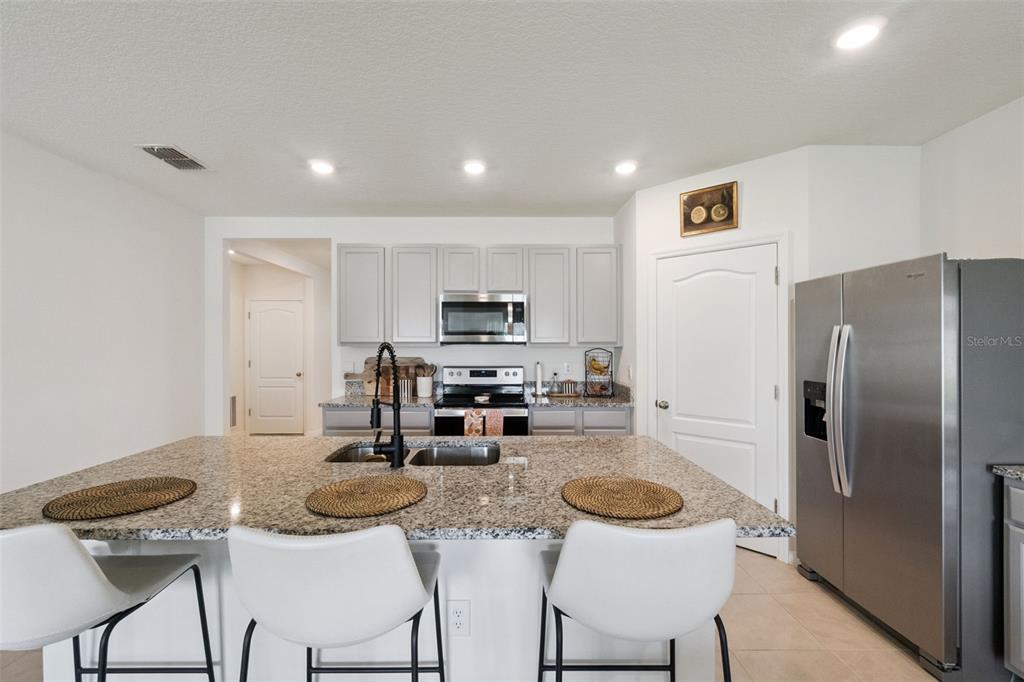 A kitchen features a granite-topped island, stainless steel appliances, and light gray cabinetry — 5805 ARBORETUM STREET, ST CLOUD, FL