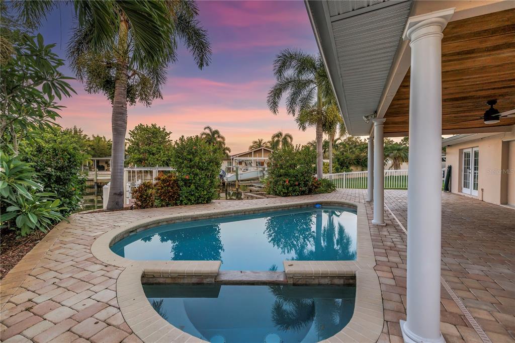 A paved patio with a covered porch overlooks a swimming pool at sunset — 1820 TANGLEWOOD DRIVE NE, ST PETERSBURG, FL