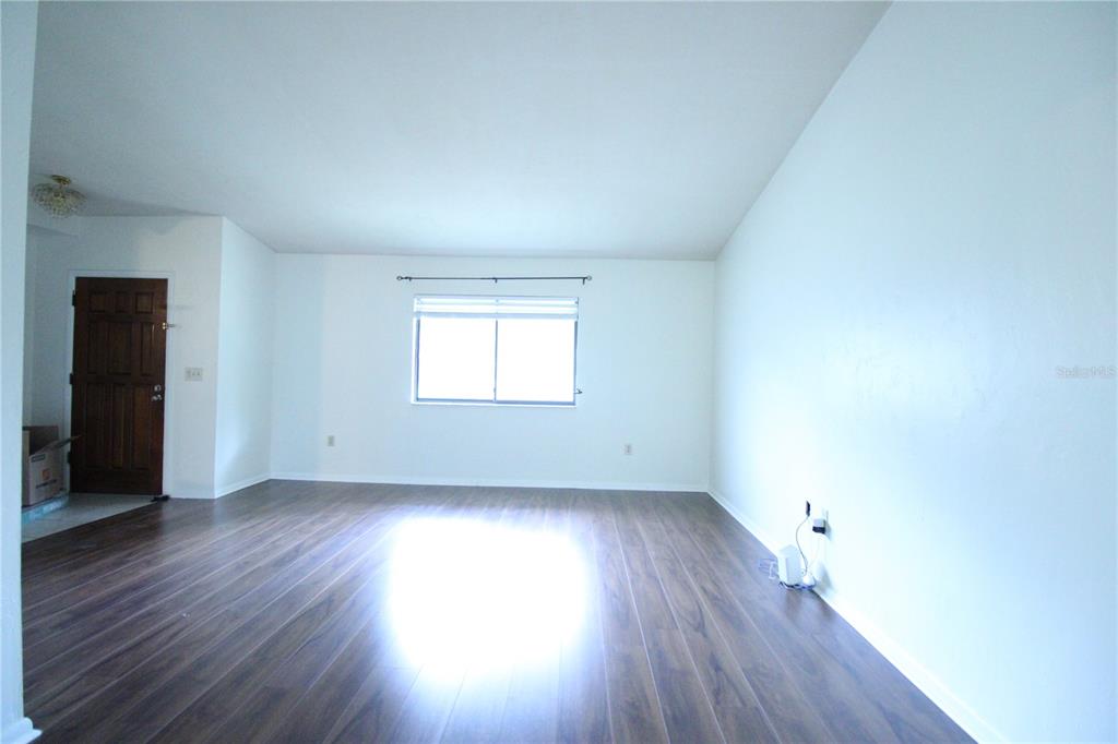 An empty living room features wood-look laminate flooring, white walls, and a single window — 1624 SW 77TH TERRACE, GAINESVILLE, FL