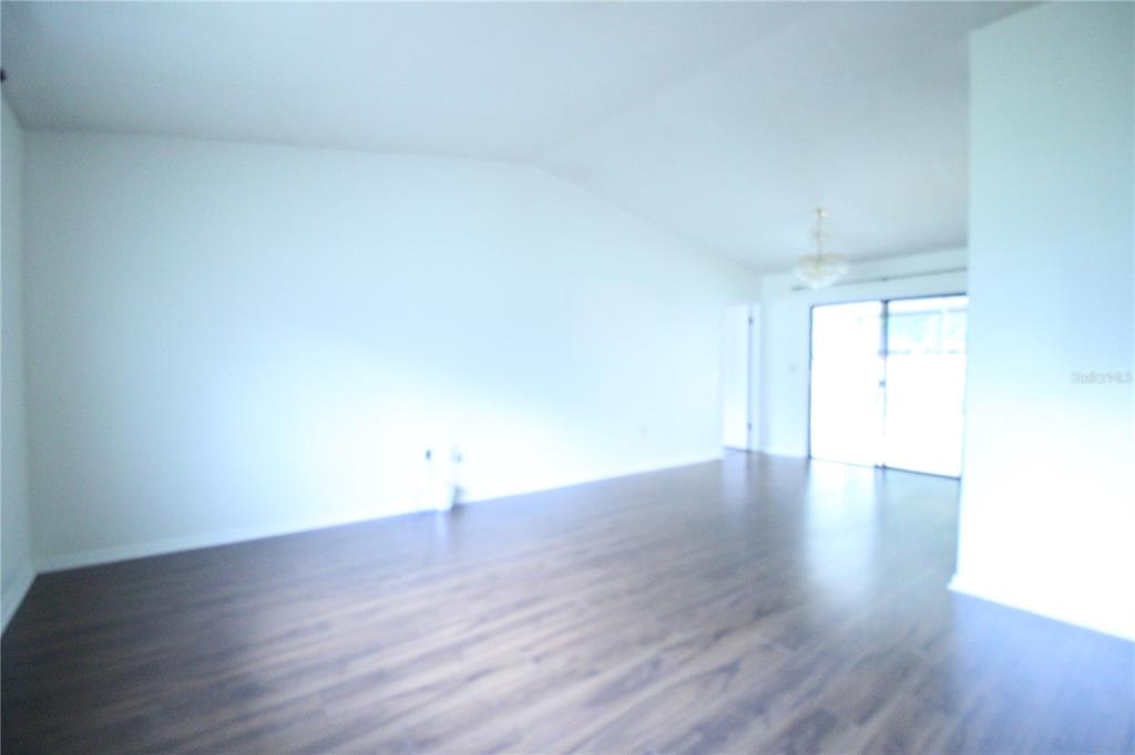 An empty room features white walls, dark wood-look flooring, and a sliding glass door — 1624 SW 77TH TERRACE, GAINESVILLE, FL