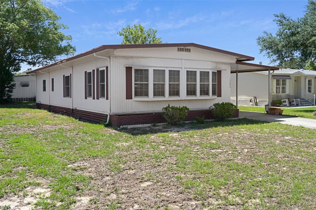 A single-story mobile home with white siding, brown shutters, and a covered carport — 15299 BROOKRIDGE BOULEVARD, BROOKSVILLE, FL
