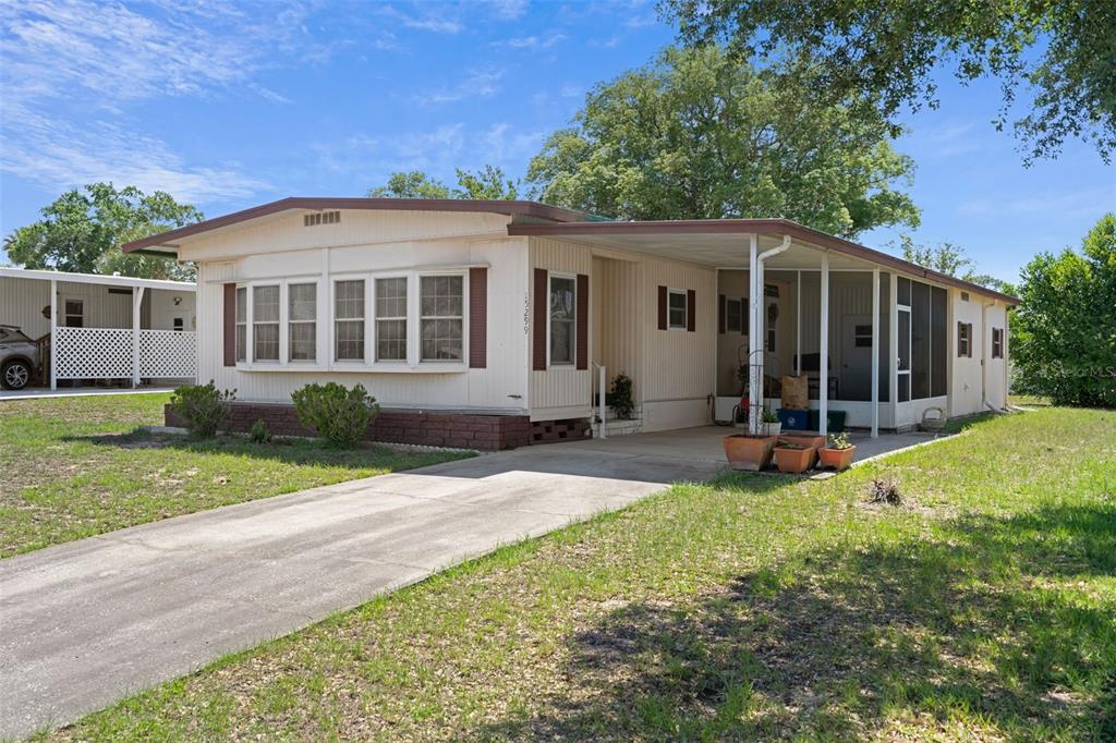 A single-story manufactured home with a concrete driveway, carport, and screened-in porch — 15299 BROOKRIDGE BOULEVARD, BROOKSVILLE, FL