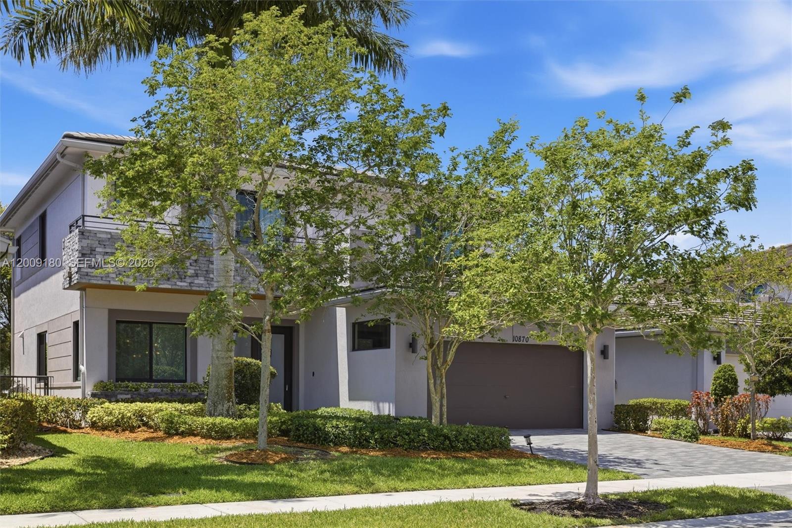 A two-story house features a stone-accented balcony, a garage, and landscaped front yard — 10870 Windward St, Parkland FL 33076, PARKLAND, FL