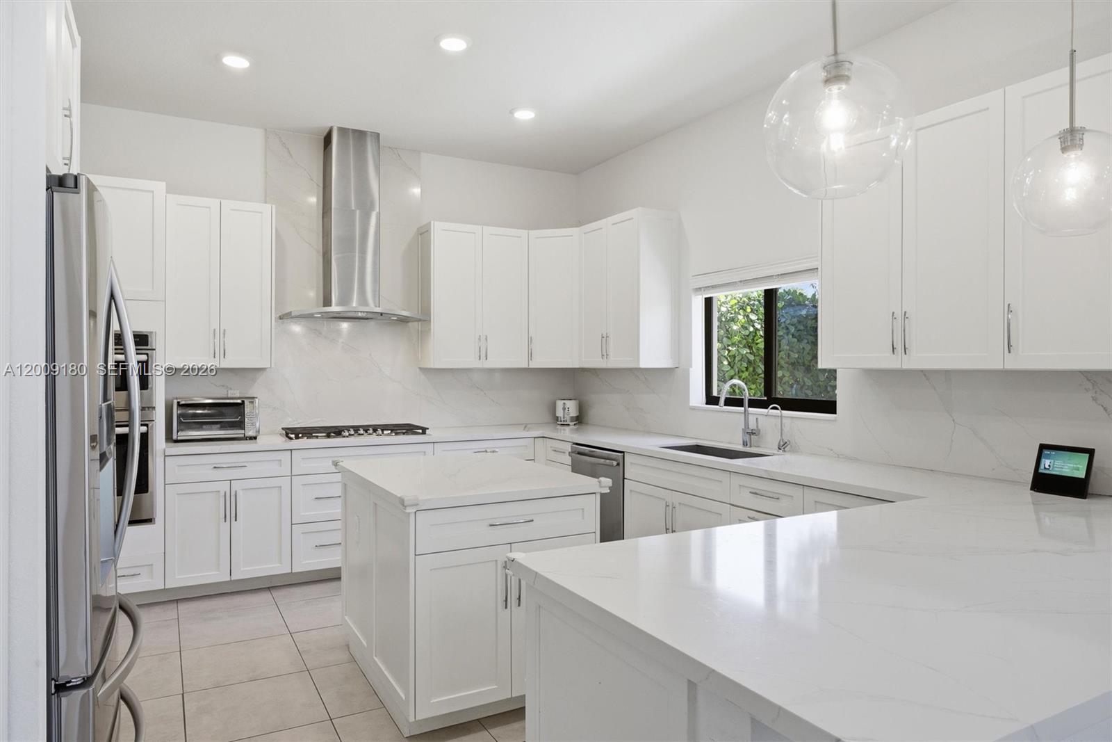 A modern white kitchen features marble-style countertops, stainless steel appliances, and a central island — 10870 Windward St, Parkland FL 33076, PARKLAND, FL