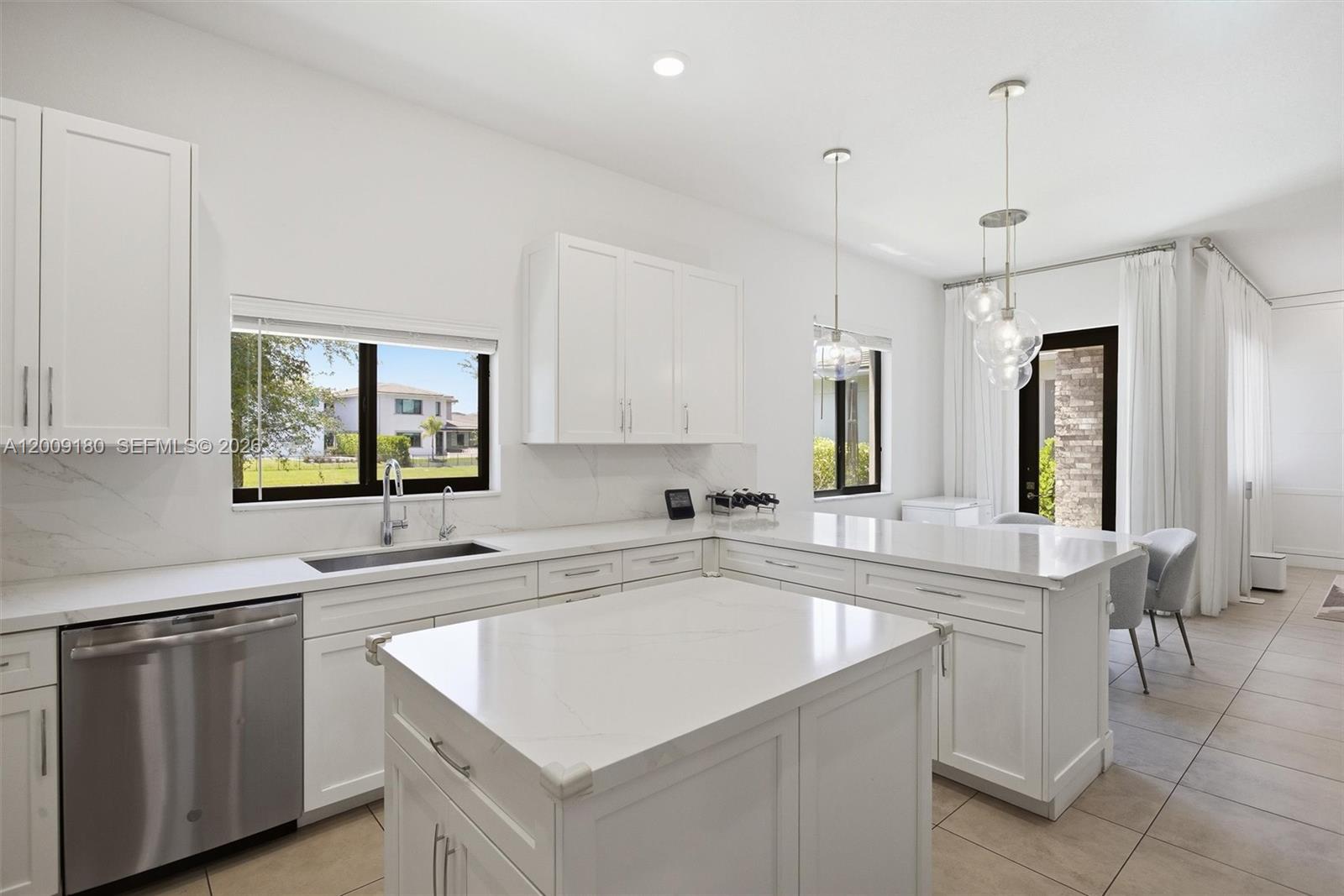 A modern white kitchen features marble countertops, stainless steel appliances, and a central island — 10870 Windward St, Parkland FL 33076, PARKLAND, FL